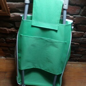 May include: A green folding wagon with a white trim and two pockets. The wagon has a handle and is made of fabric.