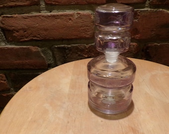 May include: A clear glass bottle with a purple tint and a textured design. The bottle has a stopper with a similar design.