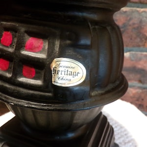 Op de afbeelding: Zwarte keramische kachel met rode accenten en een gouden label met de tekst "Genuine Heritage China".