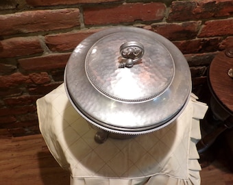 Pode incluir: Balde de gelo de metal martelado prateado com tampa e botão decorativo. O balde tem uma borda com contas e fica em três pés.