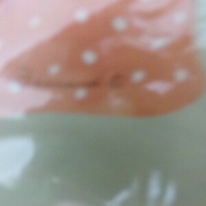 May include: A close-up of a light pink and white patterned fabric with a subtle texture. The fabric has a soft, blurred appearance.
