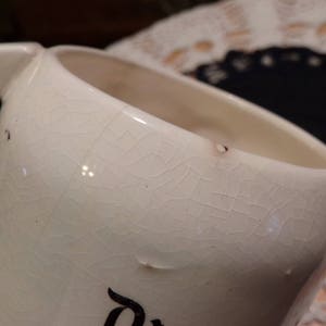 Puede incluir: Taza de cer&aacute;mica blanca con un acabado de esmalte craquelado. La taza tiene un asa y una forma redondeada.