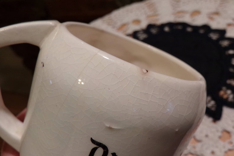 Puede incluir: Taza de cer&aacute;mica blanca con un acabado de esmalte craquelado. La taza tiene un asa y una forma redondeada.