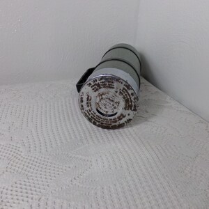 May include: A vintage silver and green thermos with a black handle and a label with text on the bottom.