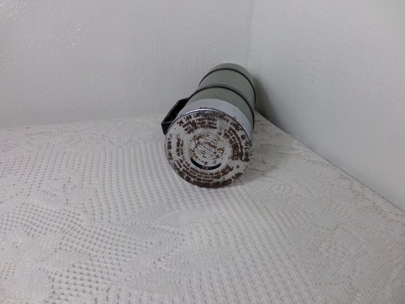 May include: A vintage silver and green thermos with a black handle and a label with text on the bottom.