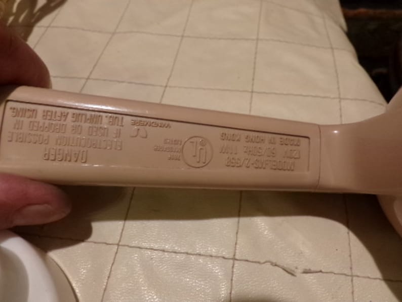 May include: A beige plastic electrical appliance with a warning label that reads "DANGER Electrocution Possible If Used or Dropped in Tub. Unplug After Using." The label also includes the text "MODELAG-2/960 MADE IN HONG KONG UL LISTED", and a UL symbol.