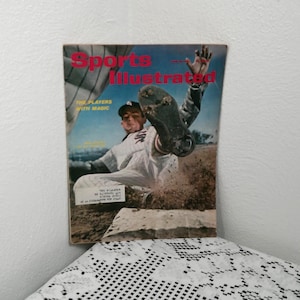 Könnte beinhalten: Vintage Sports Illustrated-Magazin-Cover mit einem Baseballspieler, der in die Base rutscht. Das Cover trägt den Titel "Sports Illustrated" in Rot und den Text "The Players With Magic". Der Spieler trägt eine weiße Uniform.
