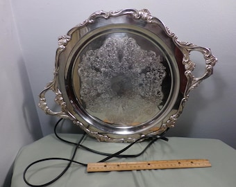 Può includere: Un vassoio da portata in argento con manici decorati e un motivo in rilievo decorativo. Il vassoio è rotondo e ha un diametro di circa 30 cm.
