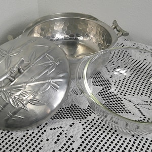 Peut inclure: Un plat de service en métal argenté avec un couvercle orné d'un motif de bambou, un plat en verre transparent et un saladier en métal argenté avec des poignées. Le saladier a une texture martelée.