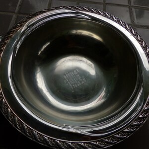 May include: A silver serving bowl with a decorative rim and an inscription on the bottom. The inscription reads "Wallace Sterling, 1940,  Made in USA".
