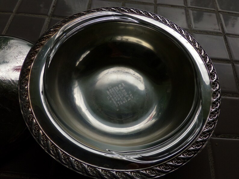 May include: A silver serving bowl with a decorative rim and an inscription on the bottom. The inscription reads "Wallace Sterling, 1940,  Made in USA".
