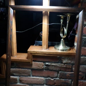 May include: A dark wood picture frame with a brass candlestick on a shelf. The shelf is made of wood and is attached to a brick wall.