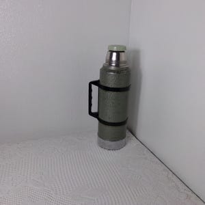 May include: A green and silver thermos with a black handle. The thermos has a speckled finish.