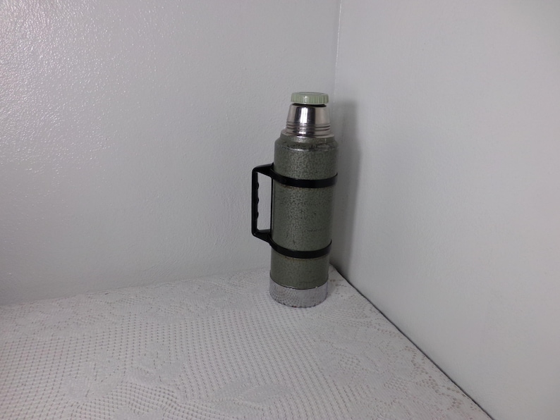May include: A green and silver thermos with a black handle. The thermos has a speckled finish.