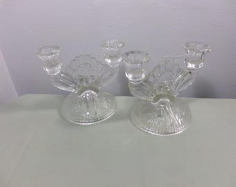May include: Two clear glass candle holders with a decorative floral design. Each holder has three candle cups and a wide base.