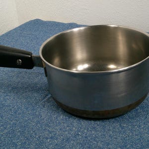 May include: A stainless steel saucepan with a black handle and a metal loop. The pot has a silver interior and a slightly browned base. The handle is attached with rivets. The saucepan is on a blue surface.