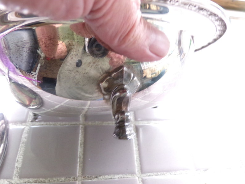 May include: Silver serving dish with a round, shallow bowl and a single, ornate foot. The dish has a beaded edge and a reflective surface.