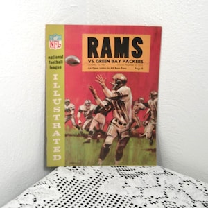 May include: Vintage NFL Illustrated magazine cover featuring the Rams vs. Green Bay Packers. The cover has a red background with the word "RAMS" in large yellow letters. The cover also features football players in action and the NFL logo.