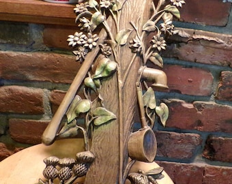 May include: A wooden wall sculpture depicting a tree trunk with leaves, vines, and a small wooden bucket. The sculpture is painted in shades of brown, green, and beige.