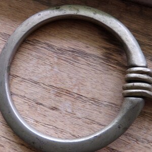 May include: A silver metal ring with a braided chain attached. The ring is smooth and has a rounded shape.