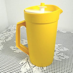 May include: A bright yellow plastic pitcher with a matching handle and lid. The pitcher has a white lid insert and a spout for easy pouring. This vintage kitchenware item is ideal for serving cold beverages.