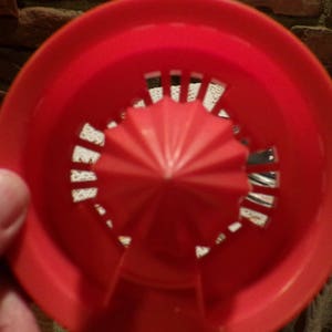 Może przedstawiać: Czerwony plastikowy wyciskacz do cytrus&oacute;w z gwiazdkowym wzorem i białą plastikową podstawą.