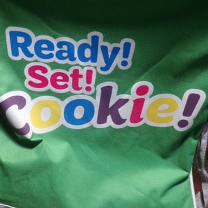 May include: Green canvas bag with the text "Ready! Set! Cookie!" in colourful letters.