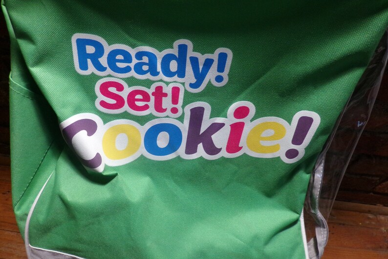 May include: Green canvas bag with the text "Ready! Set! Cookie!" in colourful letters.