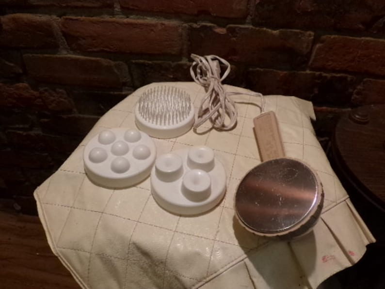 May include: A set of white massage attachments for a handheld massager. The attachments include a round brush, a round head with multiple nubs, and a round head with four nubs. The attachments are on a white surface.