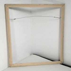 May include: A rectangular, light-colored wooden picture frame with a wire for hanging. The frame is empty, showing the back and the inside edges. The frame is set against a white background.