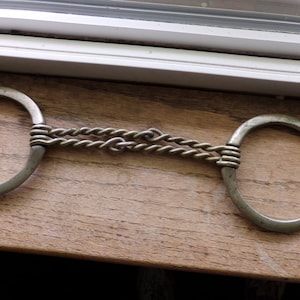 May include: A silver metal horse bit with a braided chain connecting two circular rings.