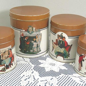 Peut inclure: Ensemble de quatre boîtes de cuisine vintage avec des couvercles marron et des corps blancs. Chaque boîte présente une illustration différente de personnes en costumes d'époque. Les boîtes sont disposées sur une nappe en dentelle blanche.