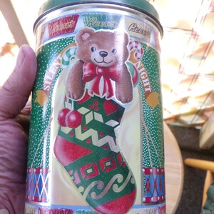 May include: A green and gold metal tin with a Christmas theme. It features a teddy bear wearing a red and gold bow tie and a stocking with a green and red pattern. The text on the tin says "Silent Night" and "Reese's".