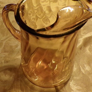 May include: Amber glass pitcher with a wide mouth and a handle. The pitcher has a textured, wavy design.