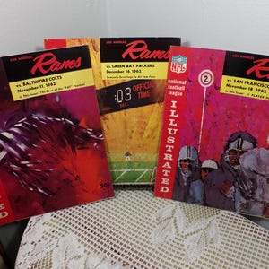 Puede incluir: Tres revistas vintage de la National Football League Illustrated con los Los Angeles Rams. Las portadas muestran el logotipo de los Rams y los oponentes del equipo: Baltimore Colts, Green Bay Packers y San Francisco 49ers. Las revistas son del 11 de noviembre de 1962, 16 de diciembre de 1962 y 18 de noviembre de 1962.