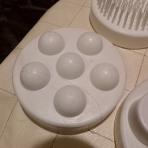 May include: White plastic facial massager with five round bumps. The massager is designed to be used on the face and neck.