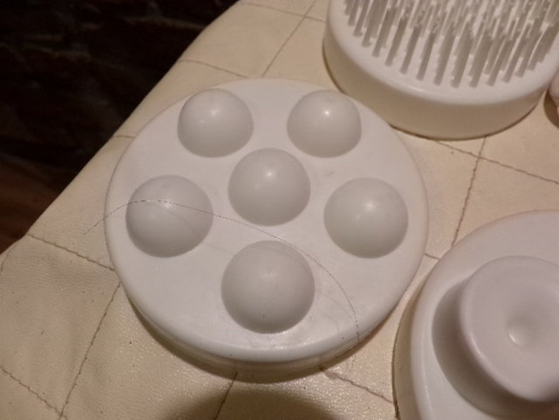 May include: White plastic facial massager with five round bumps. The massager is designed to be used on the face and neck.