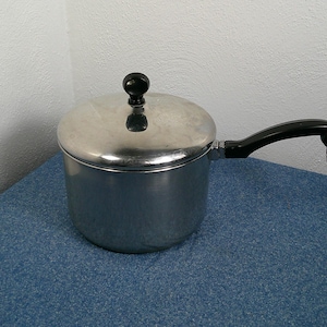 May include: A stainless steel saucepan with a lid and a black handle. The pot is on a blue surface. The handle has a loop at the end. The lid has a black knob.