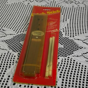 May include: A package of Chicago Cutlery Chop Stick brand chopsticks. The package is red and contains a brown chopstick holder and two chopsticks. The package is on a white lace tablecloth.