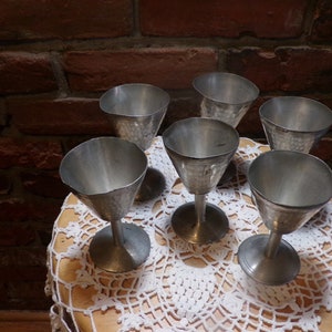 May include: Set of six silver goblets with a hammered finish, arranged on a white crocheted doily.