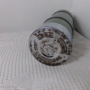 May include: A vintage metal thermos with a silver and green exterior. The thermos has a round bottom and a screw-on lid. The lid has a circular opening with a small hole in the center. The thermos is covered in rust and has a label with text that is difficult to read.