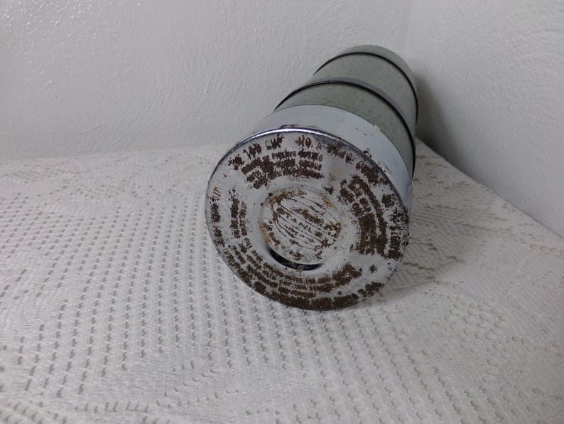 May include: A vintage metal thermos with a silver and green exterior. The thermos has a round bottom and a screw-on lid. The lid has a circular opening with a small hole in the center. The thermos is covered in rust and has a label with text that is difficult to read.