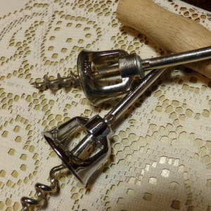 May include: Two silver metal corkscrews with wooden handles. The corkscrews are lying on a white crocheted tablecloth.