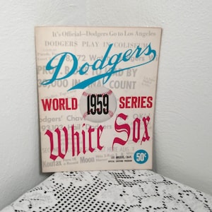 May include: Vintage 1959 World Series program featuring the Dodgers and White Sox. The cover has the Dodgers logo in blue, the words "World Series" in red, and a baseball with "1959" on it. The program is a collectible item.