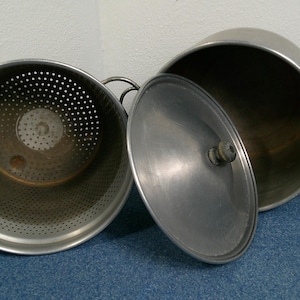 Puede incluir: Un juego de ollas de cocina de metal vintage. Una olla tiene un inserto perforado y la otra tiene una tapa. Las ollas son de color plateado y tienen asas. La tapa está a un lado, revelando el interior de la olla.