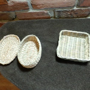 Puede incluir: Tres cestas de mimbre blancas, dos ovaladas y una rectangular. Las cestas están tejidas con un patrón blanco y marrón claro.