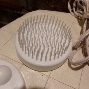 May include: A white electric foot massager with a round brush head and a white cord. The brush head has many small, white bristles.