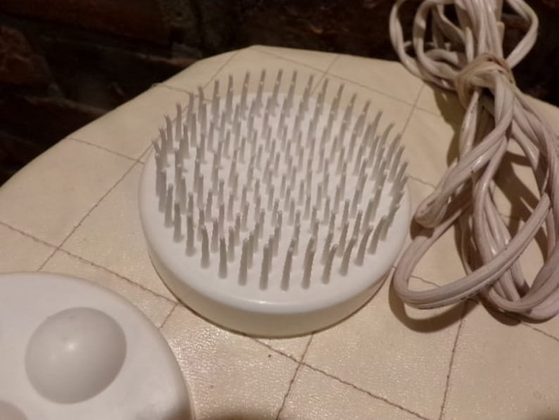 May include: A white electric foot massager with a round brush head and a white cord. The brush head has many small, white bristles.