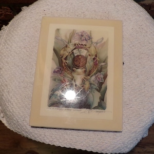 May include: A framed print featuring a whimsical design with three frogs encircling a decorative element. The artwork includes floral accents and the text "It's a Froggy Story World". The frame has a cream-colored border.