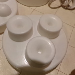 May include: White plastic base with three round attachments, each with a small hole in the centre. The base is designed to hold the attachments securely.